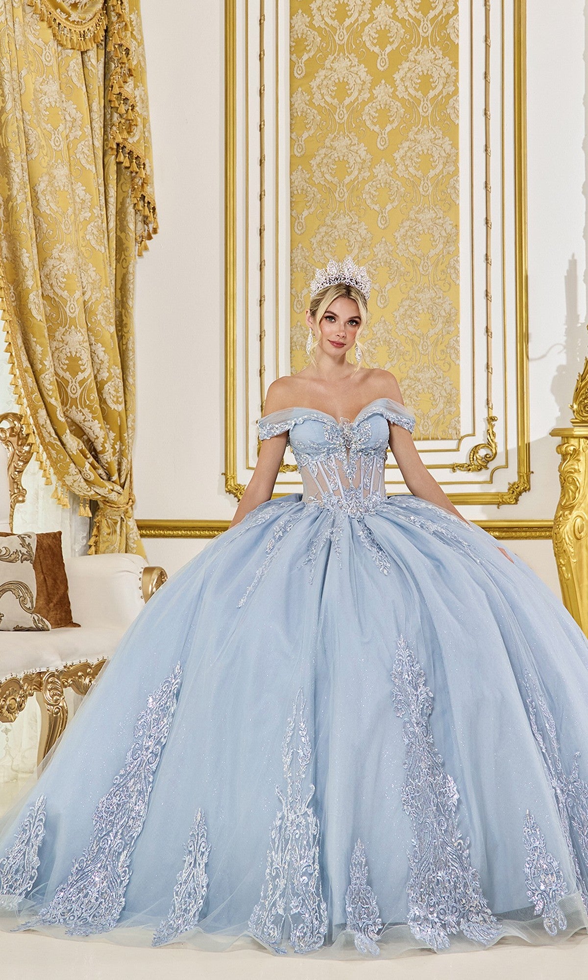 A woman in the Dusty Blue Quinceanera Dress 5089 by Dancing Queen, featuring silver embellishments and lace applique with a tiara, stands in an ornate gold and white room.